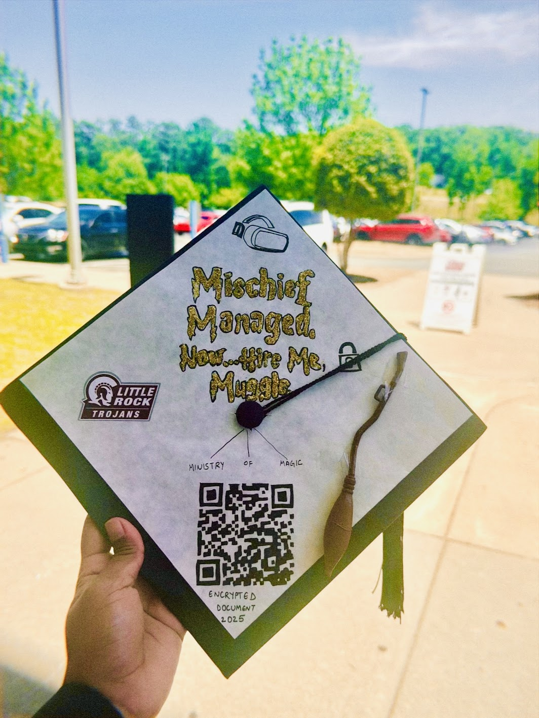 Decorated graduation cap with Mischief Managed lettering, UA Little Rock stickers, a broom, and a QR code